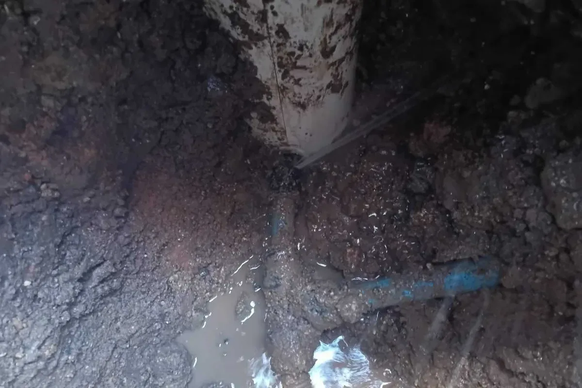 The blue supply pipe and its tee junction in the flooded excavation beside the meter box