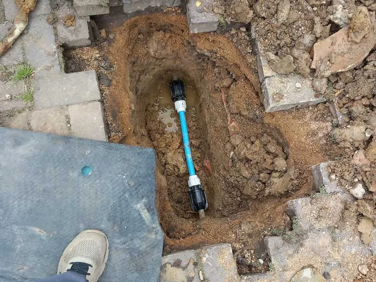 A universal transit coupling fitted to the old lead mains pipe in the excavated driveway, the repair completed